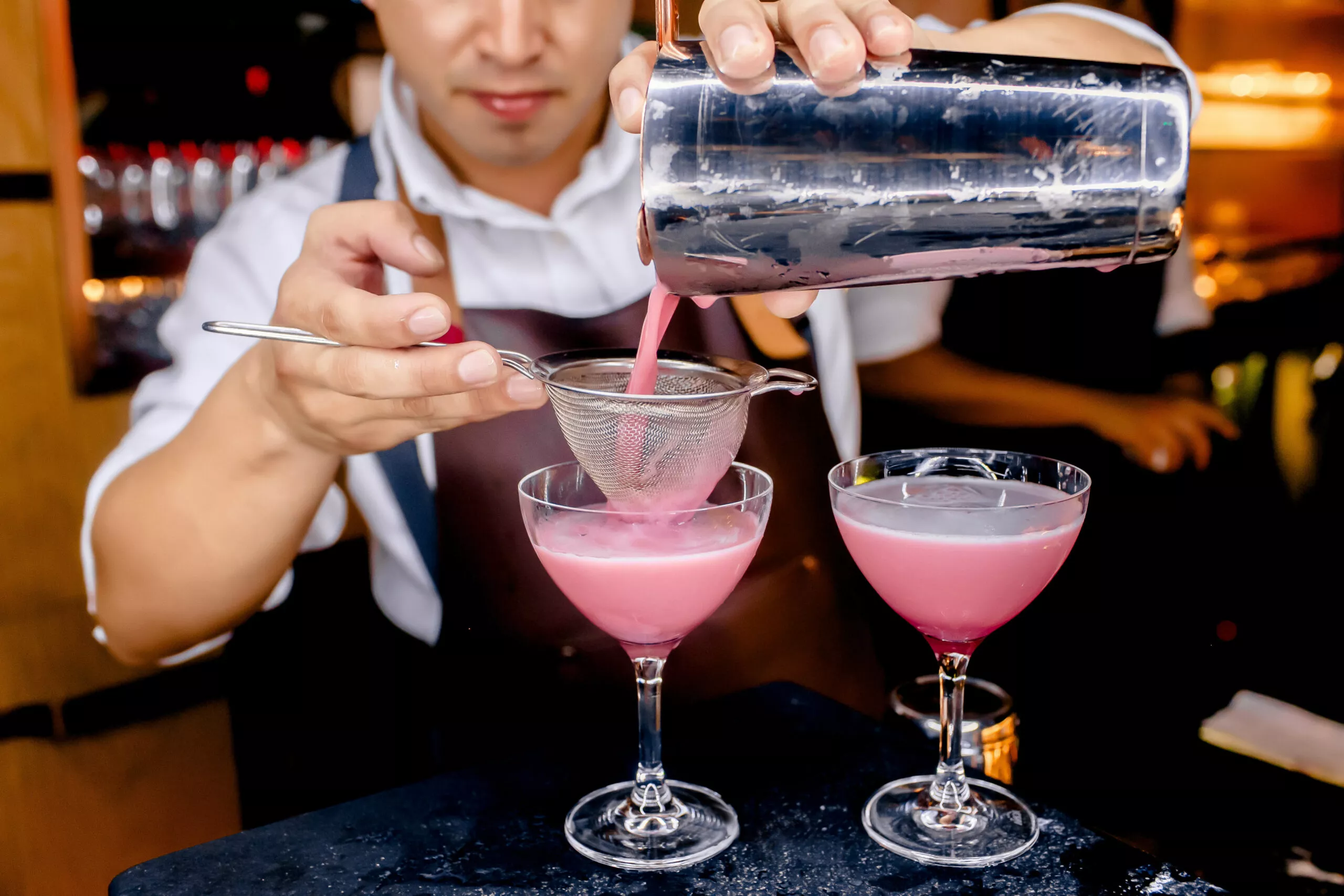 Barman die een cocktailroze drankje klaarmaakt en de alcohol inschenkt, Barman die verschillende cocktails klaarmaakt en mengt