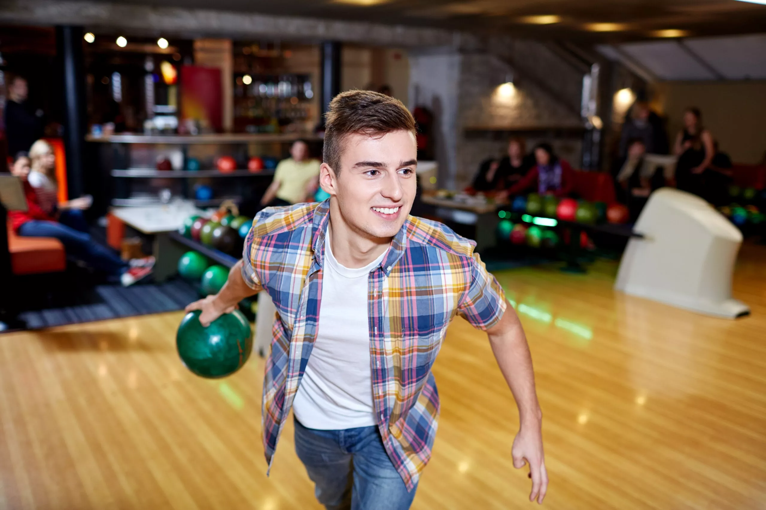 glücklicher junger Mann, der im Bowlingclub eine Kugel wirft