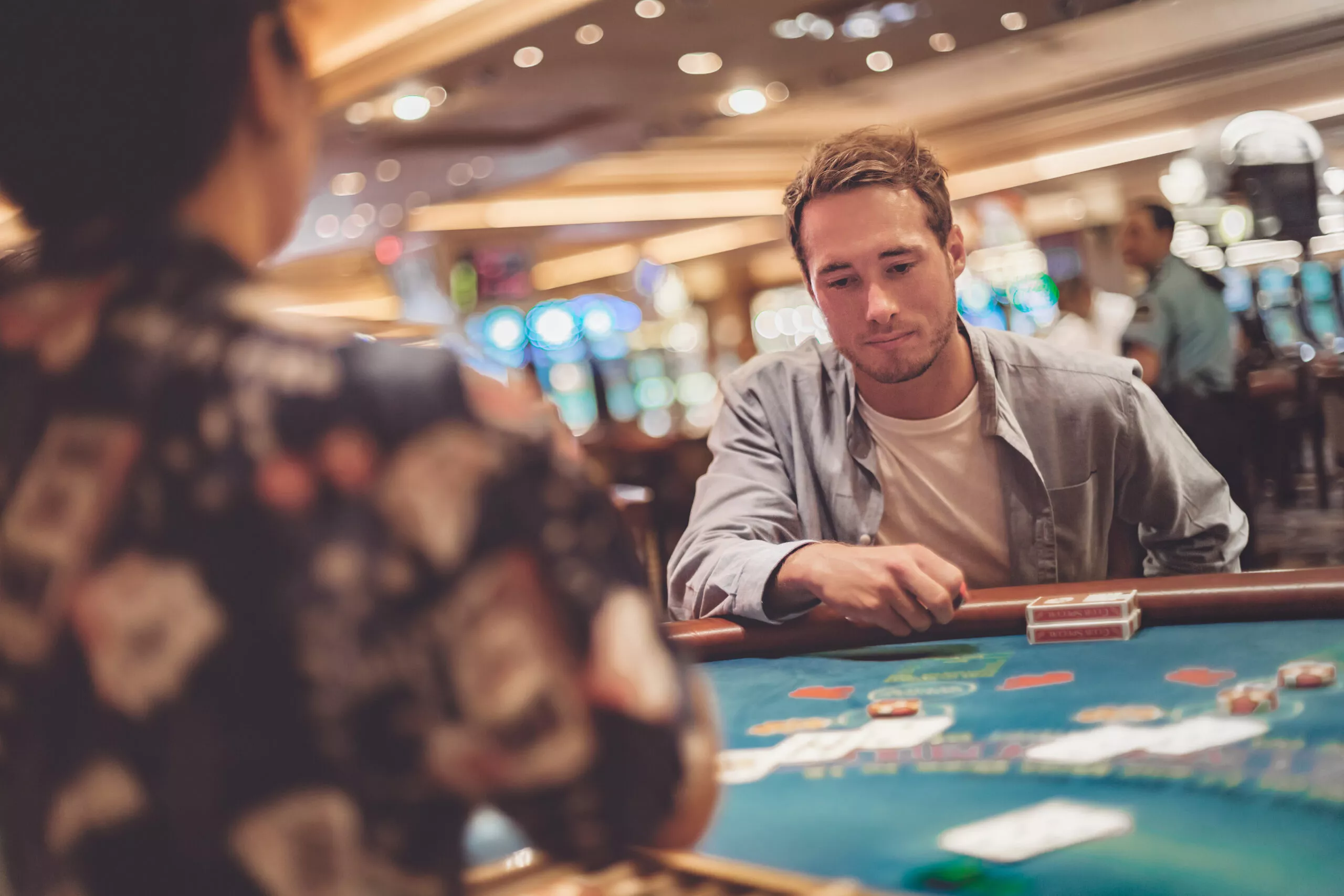 Casino gokken jonge man speelt blackjack aan tafel met kaarten en chips. Portret binnen van gokker met dealer.